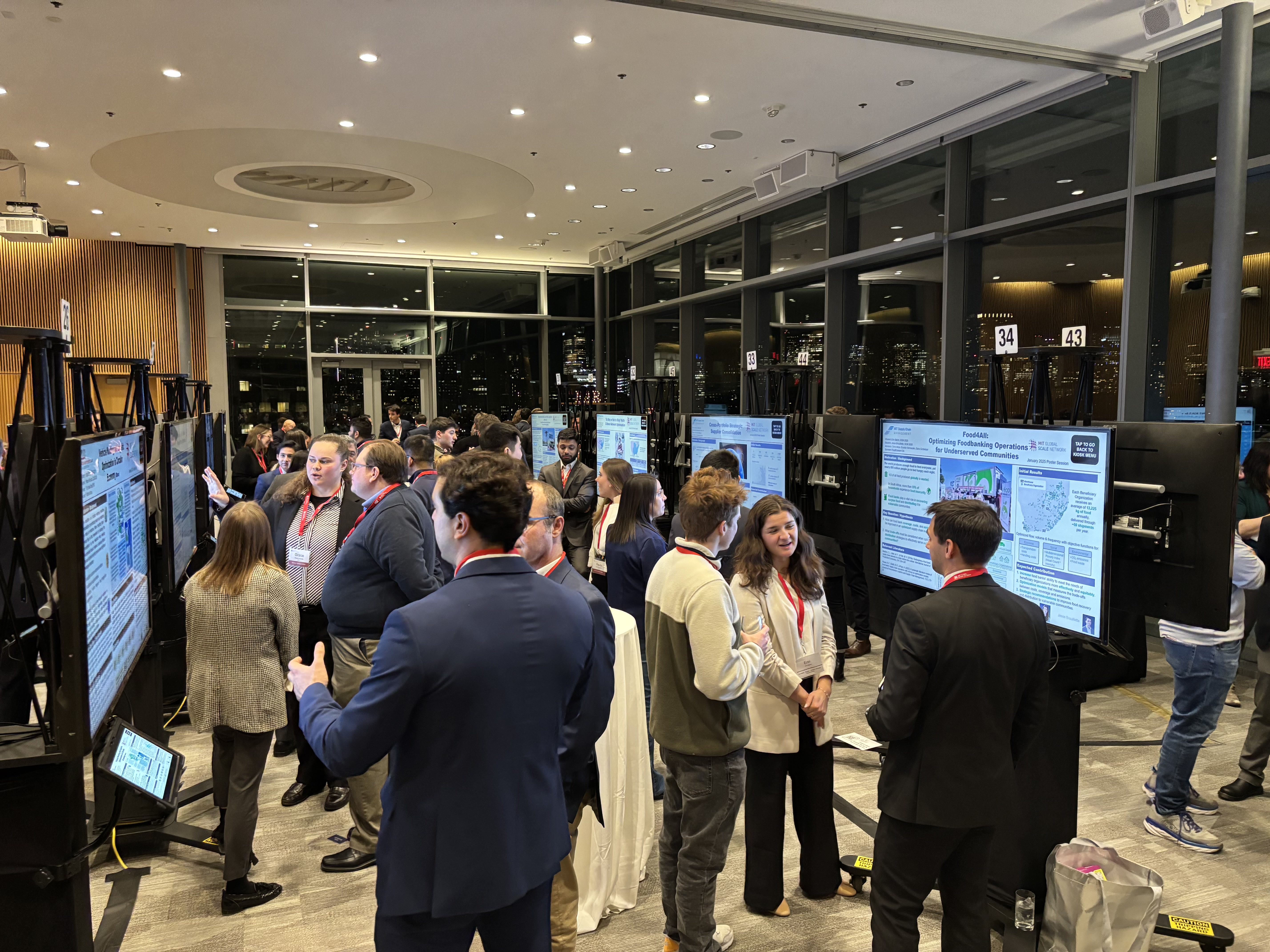 Conference attendees beside digital poster boards in a sunlit venue